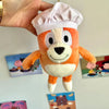 An orange and white plush doll resembling a dog wearing a white chef's hat.