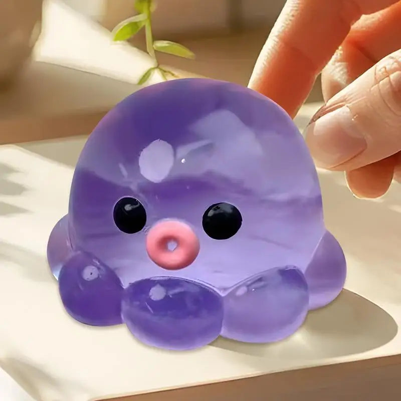 A purple octopus squishy stress ball with black eyes and a pink nose is being held by a hand.