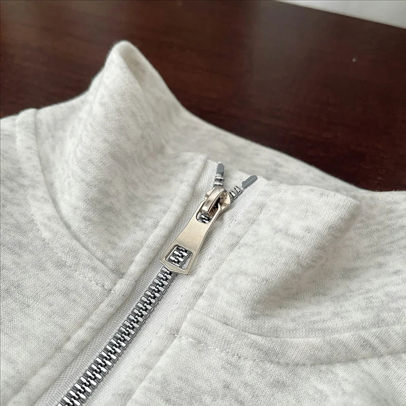 A close-up of a light gray long-sleeve sweater with a silver zipper detail on the collar.