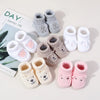 A collection of handmade knitted baby booties in various gray and pink shades are displayed next to a book.