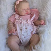 A newborn baby doll with hand-painted skin is lying in a fluffy white fur blanket.