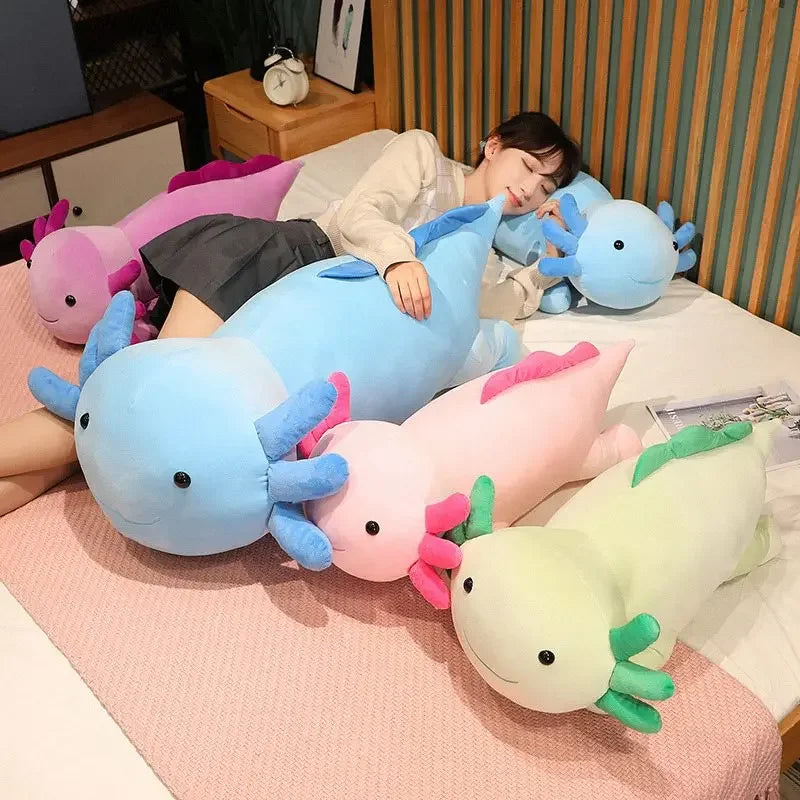 A collection of large colorful axolotl plush pillows resting on a pink surface with a person nearby.