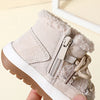 A close-up of a pair of beige baby winter snow boots with plush lining and white soles being held by a hand.