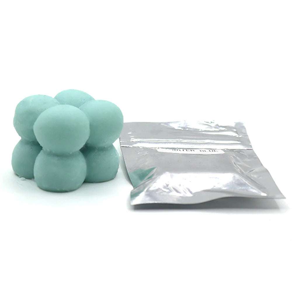 A pile of light blue candle dye chips for soy wax, beeswax, and paraffin, next to a clear plastic bag.