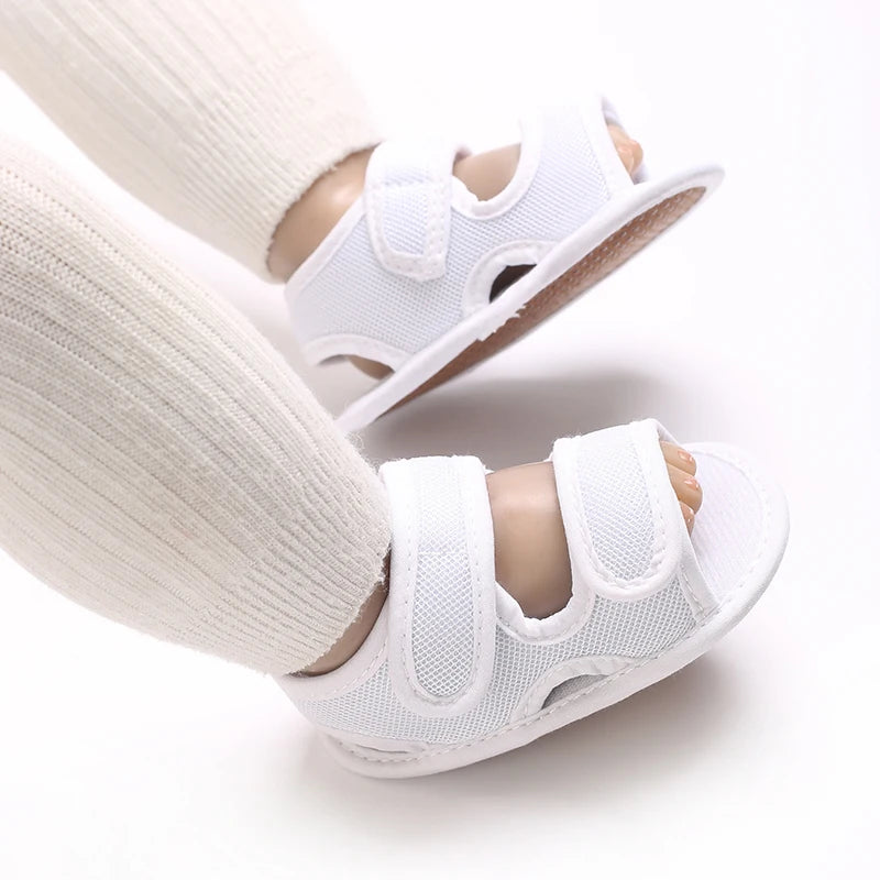White breathable first walker sandals for baby with hook-and-loop closure shown on a leg.