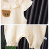 A cream-colored cotton muslin baby romper and hat set featuring a teddy bear appliqué detail.