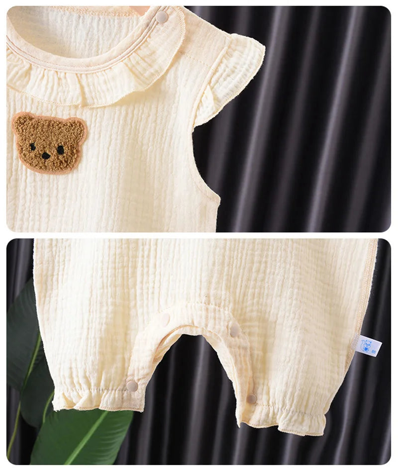 A cream-colored cotton muslin baby romper and hat set featuring a teddy bear appliqué detail.