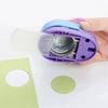 A hand holds a purple multi-size paper hole punch with a white blade, positioned above a piece of light green paper.