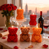 A collection of rose bear silicone candles in red, orange, and yellow are displayed on a table near a window.