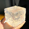 A hand holds a clear, translucent coconut oil scented squishy stress ball with an irregular geometric shape.