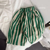 Green and beige striped cotton harem pants for kids laid out on a white surface.