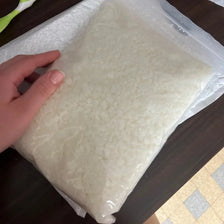 A hand holds a clear plastic bag filled with white natural beeswax pellets for DIY candle making and skincare.