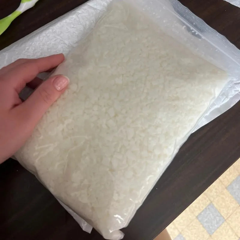 A hand holds a clear plastic bag filled with white natural beeswax pellets for DIY candle making and skincare.