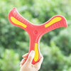 A hand holds a bright pink foam boomerang flying disc with yellow accents against a blurred green outdoor background.