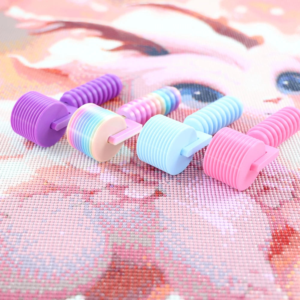 Assortment of colorful, textured rollers used for diamond painting, arranged on a pink background.