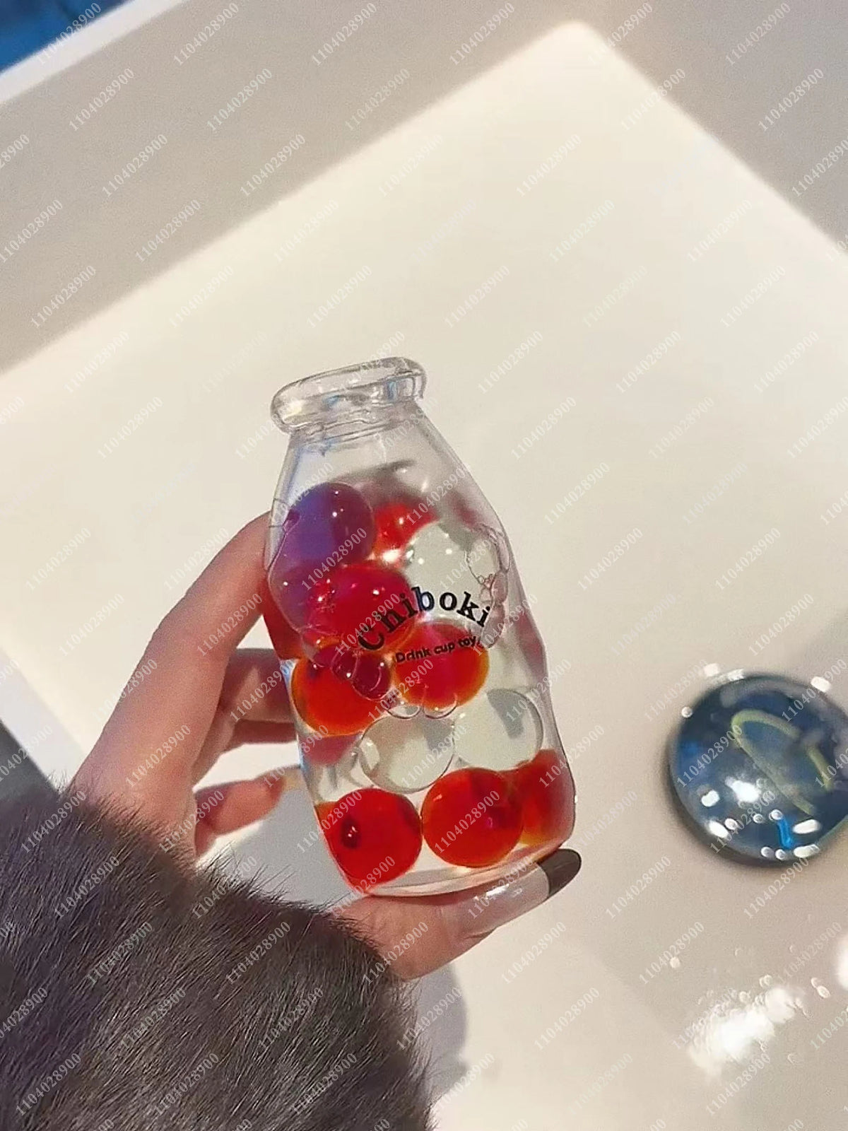 A hand holds a clear glass bottle filled with red and white squishy stress balls for sensory relaxation.