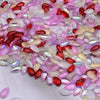 A close-up view of various iridescent pink, red, and clear water drop Czech glass beads for jewelry making.