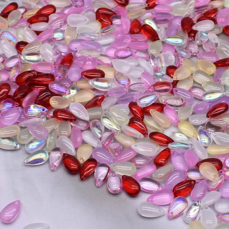 A close-up view of various iridescent pink, red, and clear water drop Czech glass beads for jewelry making.