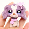 A small purple and white miniature pet animal figure with pink accessories is held in a hand.