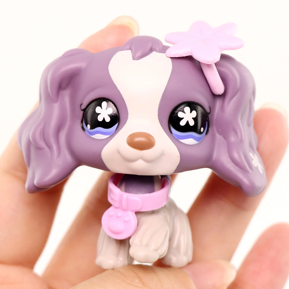 A small purple and white miniature pet animal figure with pink accessories is held in a hand.