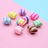 A collection of ten colorful polymer clay marshmallow charms in various stripes and swirls arranged on a pink background.