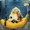 A yellow banana shaped toy featuring a plush character with large glasses and a small brown bear, suspended by a string.