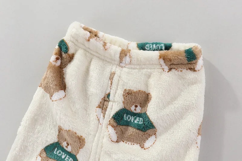A set of cream-colored fleece jacket and pants featuring brown teddy bear cartoon prints with green accents.