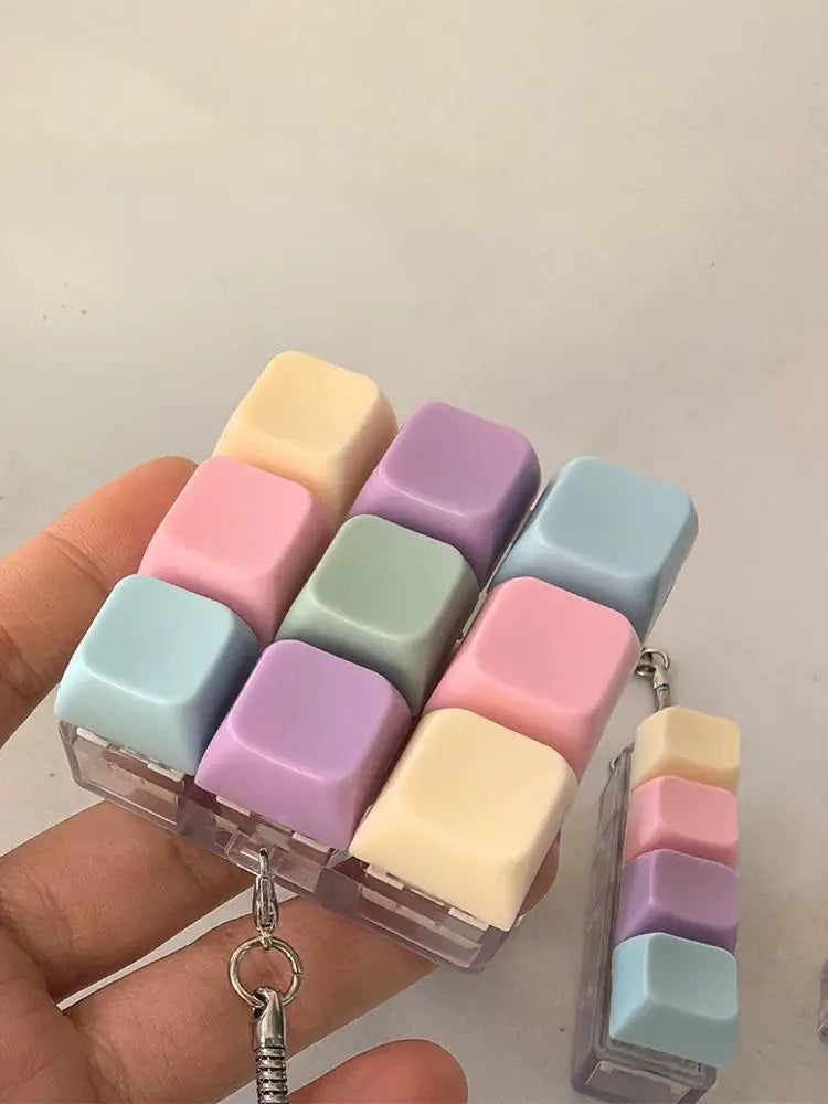 A hand holds a clear silicone pastel keyboard keychain fidget toy with various colored buttons.