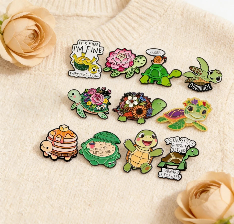 A set of cute green turtle enamel pins featuring various designs and text on a beige sweater.