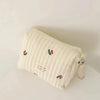 A cream quilted baby diaper caddy organizer with red floral embroidery and attached stroller straps.