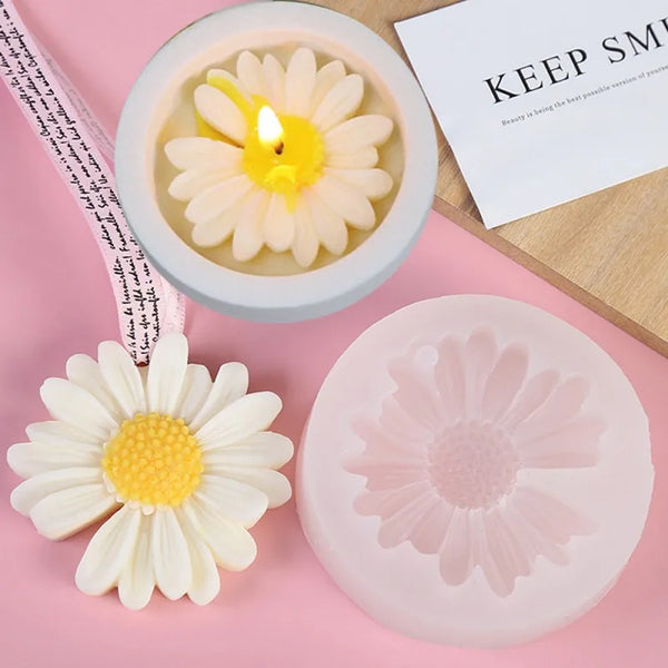 Eine weiße Silikonblumenform neben einer rosa Silikonblumenform und einer Kerze in einer Glasschale.