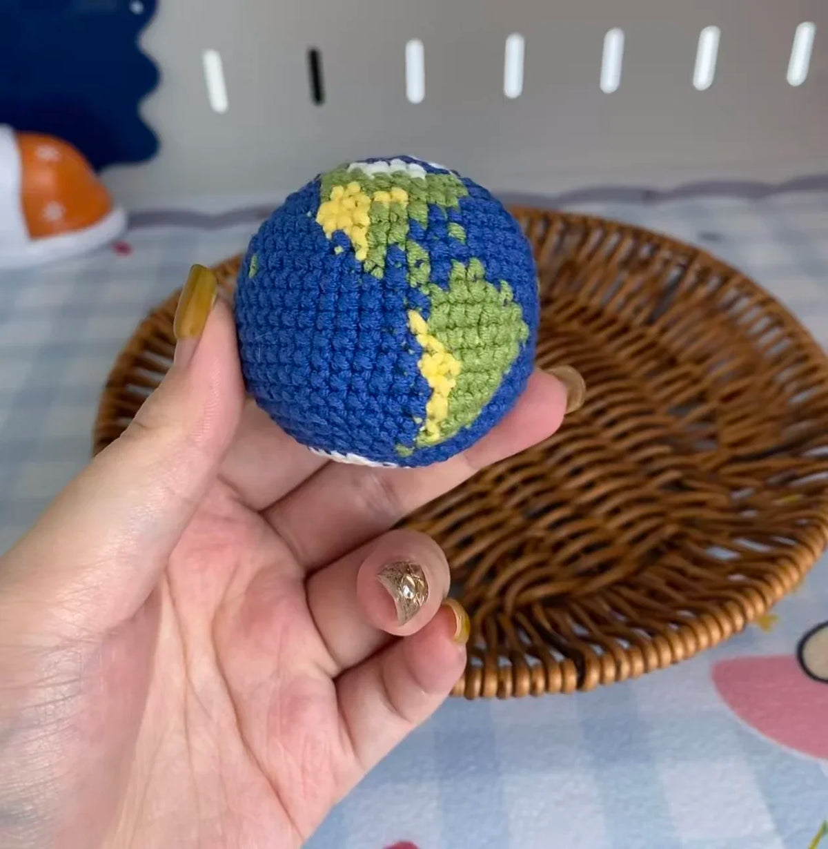 A hand holds a handcrafted crochet earth keychain charm depicting the globe in blue and green.