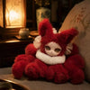 A fluffy red fox plush collectible with large eyes is displayed next to a lit lantern in a dimly lit setting.