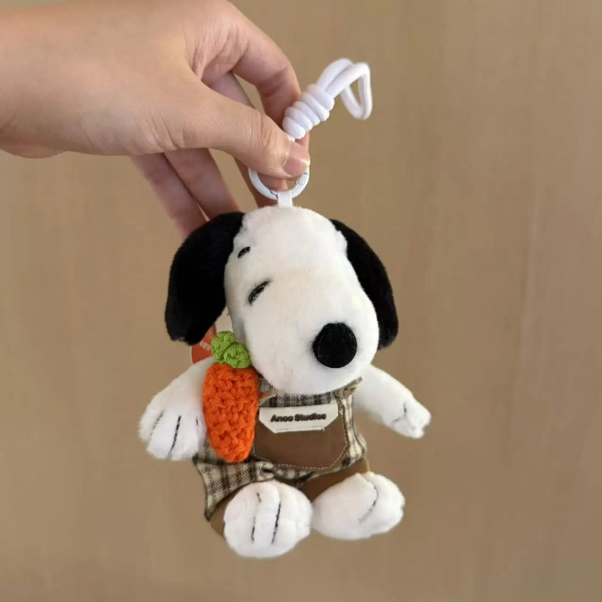 A white dog plush keychain charm with black ears and a green seed attached to a brown fabric tag