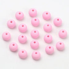 A collection of pink matte acrylic beads scattered on a white background.