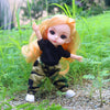 An orange-haired Articulated BJD princess doll in a black top and camouflage pants standing in green grass.