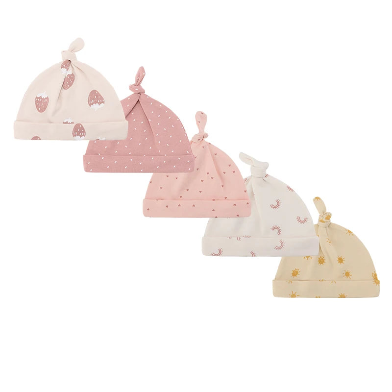 A set of four pink and cream knitted baby hats featuring strawberry, moon, and floral patterns.