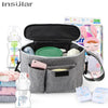 A gray stroller organizer bag with multiple compartments and bottle holders is shown next to a baby doll.