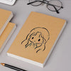 A blank kraft paper notebook with a simple line drawing of a girl's face on the cover, next to reading glasses and a pen.