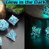 A set of blue glow-in-the-dark polyhedral dice resting on a wooden surface with a dark, glowing background.