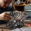 A man is assembling a detailed motorized V8 supercar engine building kit with many small parts on a wooden table.