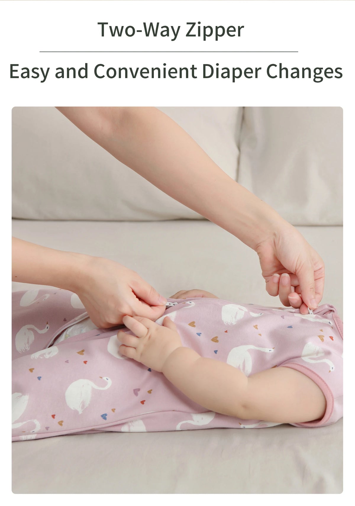 A hand is shown changing a baby diaper using a two-way zipper on a pink sleeping bag.