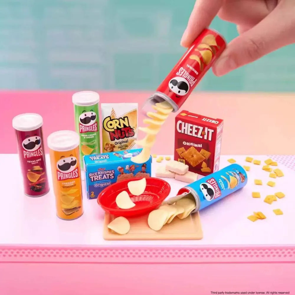 A hand is dispensing corn nuggets from a red tube into an orange container, with various snack products visible.