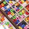A wooden tray filled with colorful acrylic letter beads in various shapes and colors for DIY jewelry making