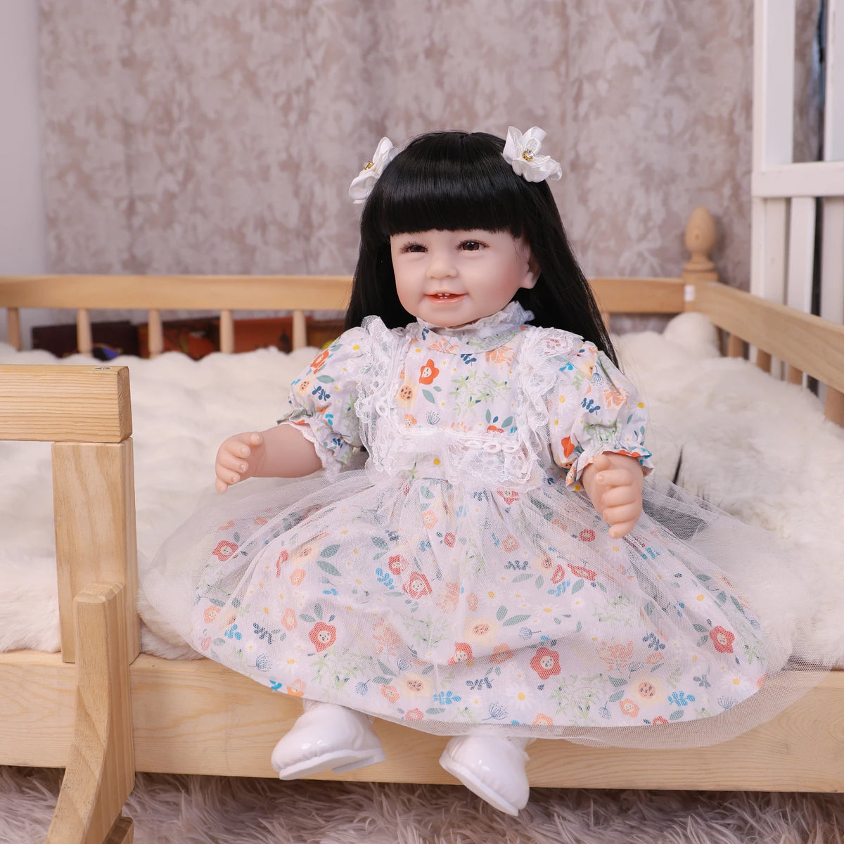 A lifelike reborn baby doll with a soft cloth body wearing a floral dress sitting in a wooden crib.