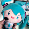 A soft teal plush doll of Hatsune Miku with pink cheeks and purple hair being held by a hand.