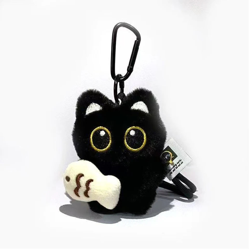 A black plush cat charm with gold eyes and a white paw visible, attached to a black keyring.