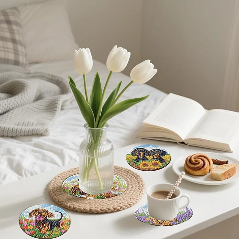 A set of DIY diamond art coasters featuring cute dog designs, displayed on a white table with a cup and a book.