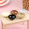 A set of ten miniature dollhouse rice bowls in various earthy and neutral tones arranged on a light wooden surface.