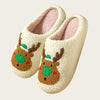 A pair of cream-colored plush indoor slippers decorated with brown reindeer faces and green accents.